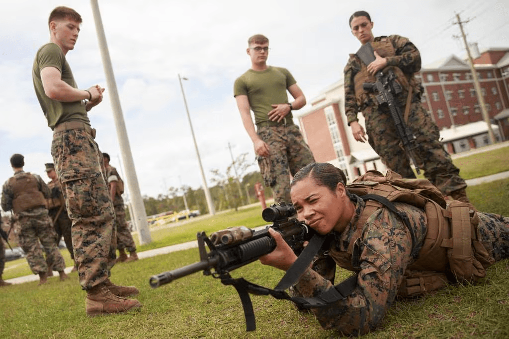 Foto de mulher em acampamento militar usando arma com homens militares em volta